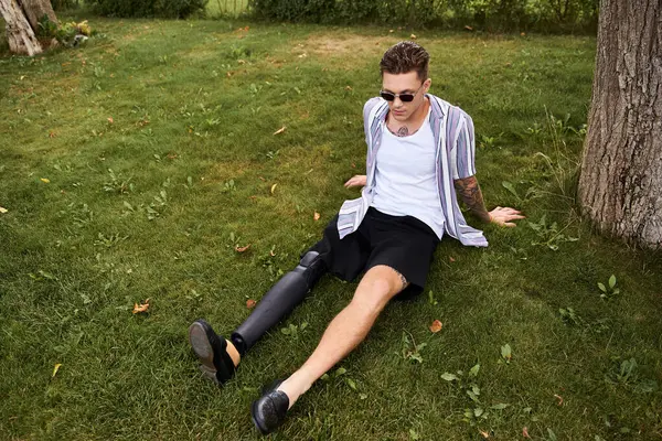 A young man in casual clothes relaxes on green grass, proudly displaying his prosthetic leg. — Stock Photo