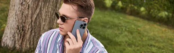 Young man with tattoos sits outdoors talking on his smartphone under the sun. — Stock Photo