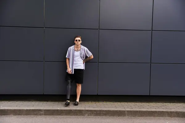 Young man with a prosthetic leg poses stylishly in front of a contemporary gray wall. — Stock Photo