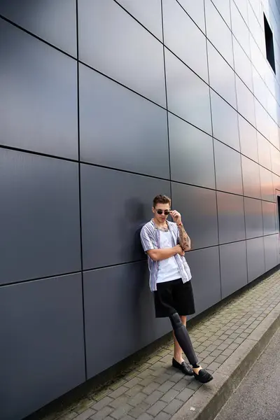 Young man with prosthetic leg stands stylishly against sleek wall in urban setting. — Stock Photo