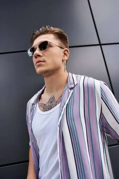 Young man with tattoos poses confidently in a trendy outfit against a modern backdrop. — Stock Photo