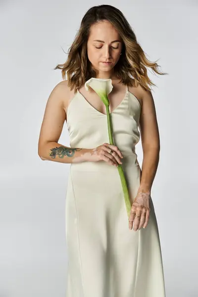 A young woman with vitiligo gently holds a calla lily while wearing a delicate outfit indoors. — Stock Photo