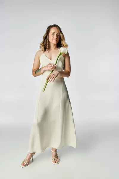 Beautiful young woman with vitiligo stands gracefully in a light dress holding a flower. — Stock Photo