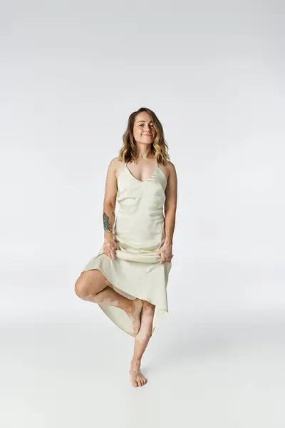 Young woman shows her unique beauty while standing elegantly on one leg in a light dress. — Stock Photo