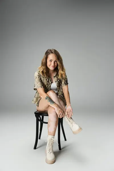 A young woman with vitiligo displays confidence while posing on a chair in a studio environment. — Stock Photo
