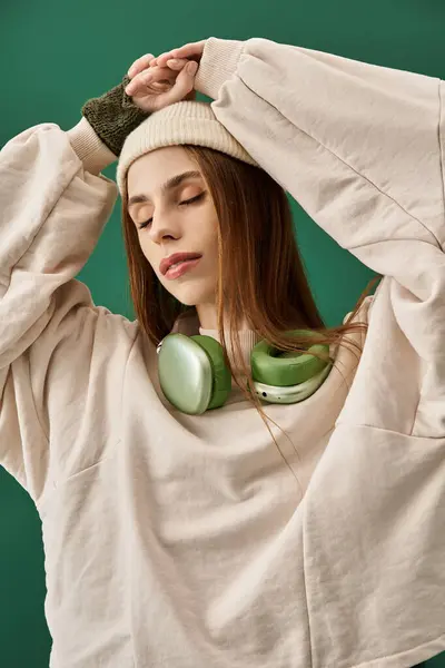 Young woman with long hair wearing a knit hat and oversized sweater listens to music thoughtfully. — Stock Photo