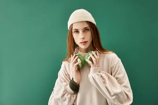 Young woman with headphones poses against a green backdrop, showcasing her beauty and strength. — Stock Photo