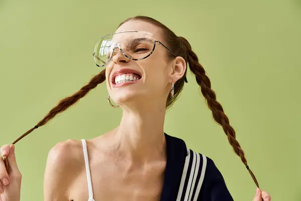 A young woman with braids expresses joy by smiling widely against a vibrant green backdrop. — Stock Photo