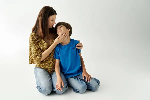 Una joven madre se arrodilla junto a su hijo, compartiendo un momento de amor en un estudio luminoso. - foto de stock