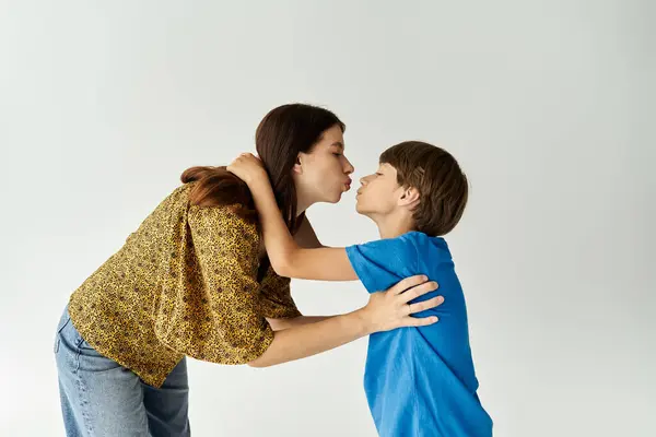 A young mother shares a tender moment, kissing her son, showcasing their close bond in a studio. — Stock Photo
