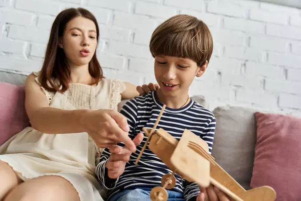 Une jeune mère et son fils partagent un moment de qualité en jouant avec un avion jouet en bois à la maison. — Photo de stock