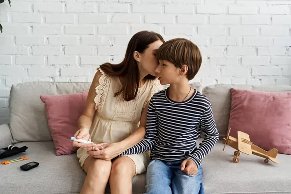 A young mother comforts her son while managing his diabetes in a cozy living room. — Stock Photo
