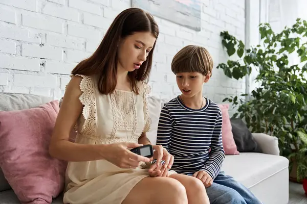 A young mother explains insulin monitoring to her son in a cozy living room setting. — Stock Photo