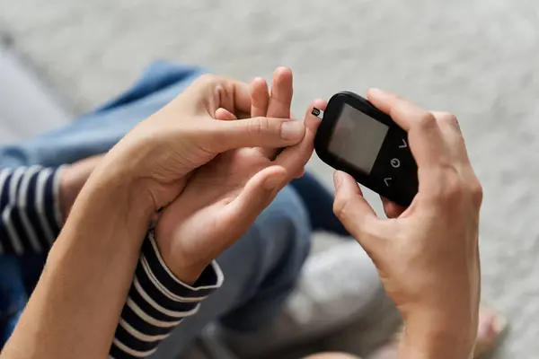 Young mother helps her son check blood sugar levels at home in their cozy living room. — Stock Photo