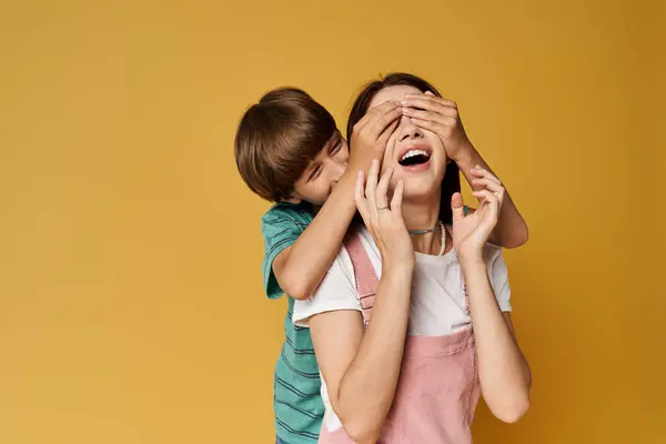 A mother shares joyful laughter with her son as he playfully covers her eyes with his hands. — Stock Photo
