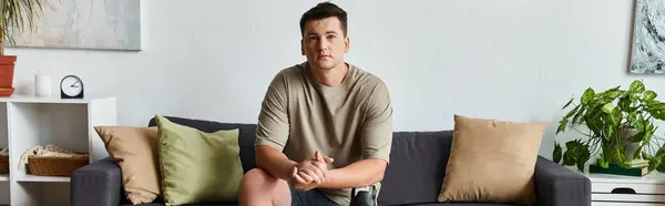 Beau jeune homme avec une jambe prothétique se détend sur un canapé dans un espace de vie moderne. — Photo de stock