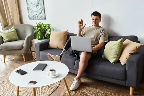 Handsome young man with prosthetic leg engages in video call from comfortable couch at home. — Stock Photo
