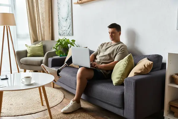 A young handsome man sits comfortably on a couch, focused on his laptop, in a modern living space. — Stock Photo