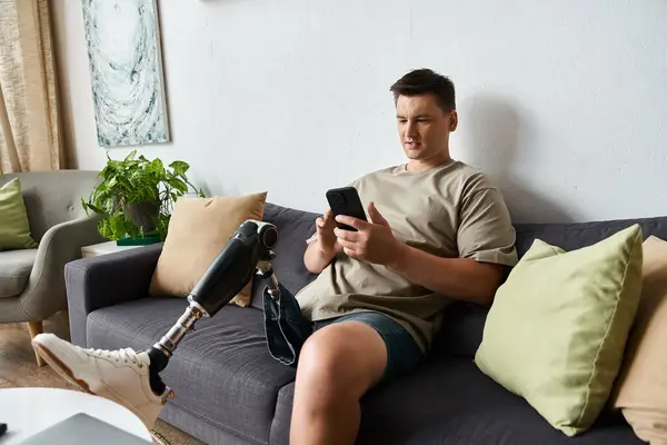 Young man with prosthetic leg relaxes on a couch, focused on his smartphone in a stylish setting. — Stock Photo