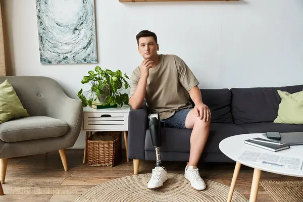 Handsome young man relaxes on a couch, hand on chin, in stylish living space. — Stock Photo