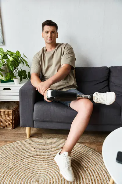 Handsome young man relaxes on a couch, showcasing his prosthetic leg in a cozy setting. — Stock Photo