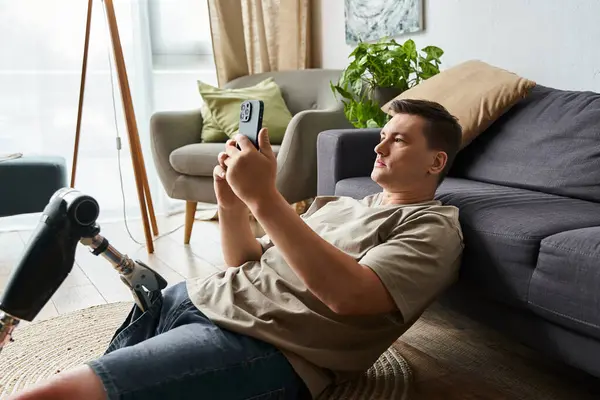 Young man sits comfortably on the floor, engaged with his smartphone, showcasing a prosthetic leg. — Stock Photo