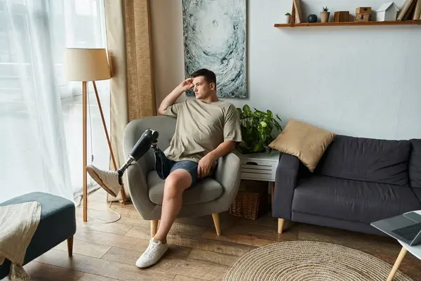 Young man enjoys a quiet moment in a stylish living room, showing his prosthetic leg. — Stock Photo