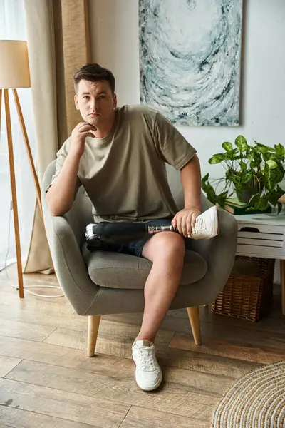 Young man poses thoughtfully on a chair, showcasing his prosthetic leg in a stylish space. — Stock Photo