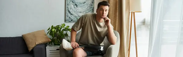 Handsome young man relaxes in a cozy living space while holding his prosthetic leg. — Stock Photo