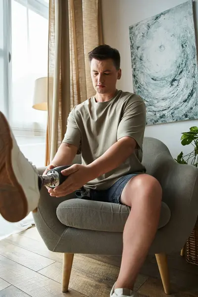 Handsome young man sits on a chair, adjusting his prosthetic leg with focus and determination. — Stock Photo