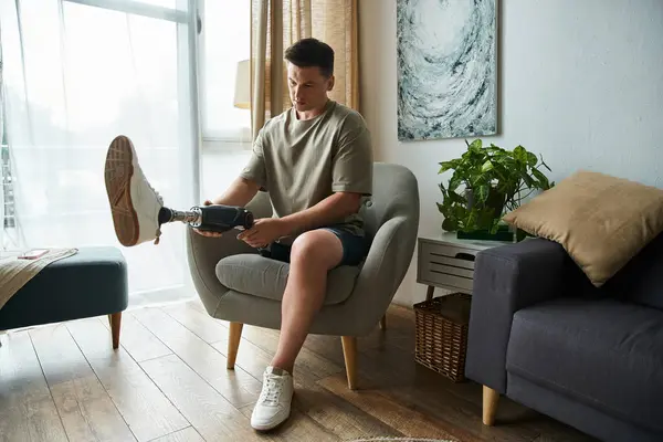 Man seated comfortably in a chair, making adjustments to his prosthetic leg indoors. — Stock Photo