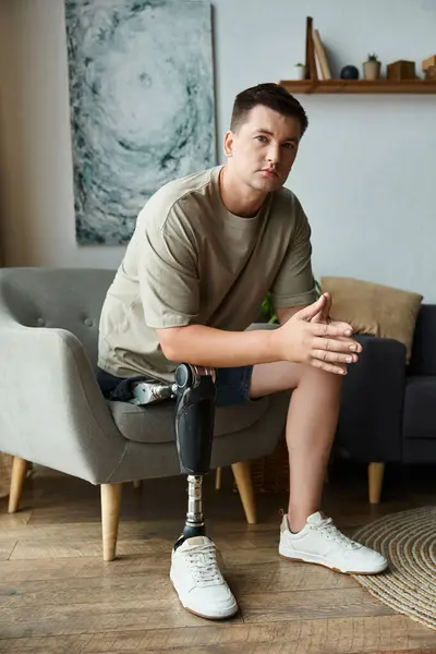 Handsome young man sits on a couch, showcasing his prosthetic leg with confidence and style. — Stock Photo