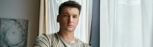 Handsome young man stands by a window, showcasing his thoughtful expression. — Stock Photo