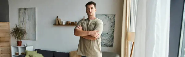 A young handsome man stands proudly with arms crossed in his stylish living room. — Stock Photo