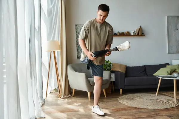 Handsome young man adjusts his prosthetic leg while standing in a stylish living room. — Stock Photo