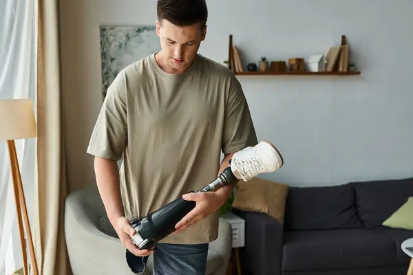 Handsome young man focuses on his prosthetic leg while standing in a modern living room — Stock Photo