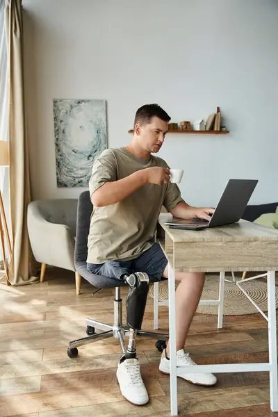 Handsome young man in casual attire sits at a desk with a laptop and coffee cup in a cozy room. — Stock Photo