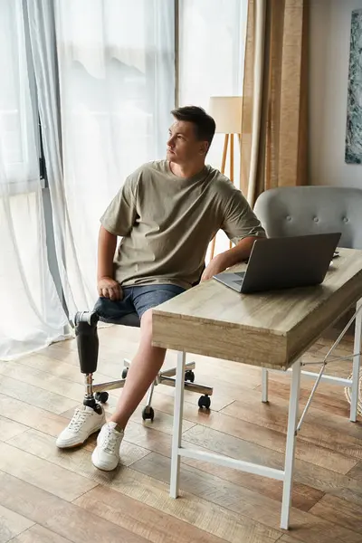 Handsome young man sits in a stylish room, focused on a laptop at a wooden desk. — Stock Photo