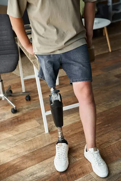 Young handsome man stands with a prosthetic leg in a stylish, contemporary office setting. — Stock Photo