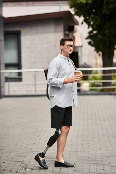Joven guapo con la pierna protésica camina con confianza mientras sostiene una taza de café. — Stock Photo