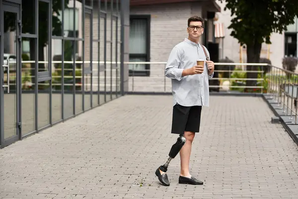 Handsome young man standing on a sidewalk with a coffee cup beside a modern establishment. — Stock Photo