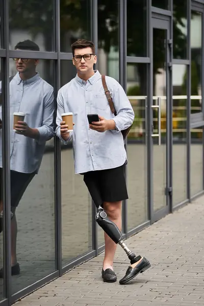 Young man sips coffee and checks his phone outside a modern building. — Stock Photo