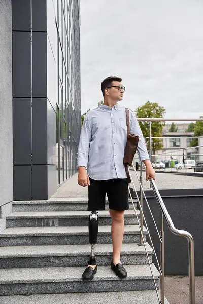 Un joven guapo con una pierna protésica se para en las escaleras fuera de un edificio moderno. - foto de stock