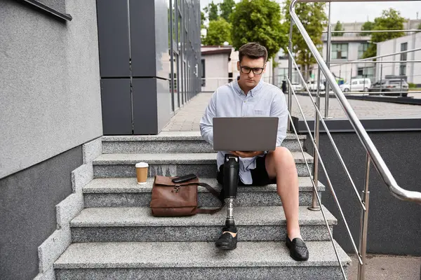 Handsome young man sits on stairs, using laptop and enjoying coffee in a modern city environment. — Stock Photo