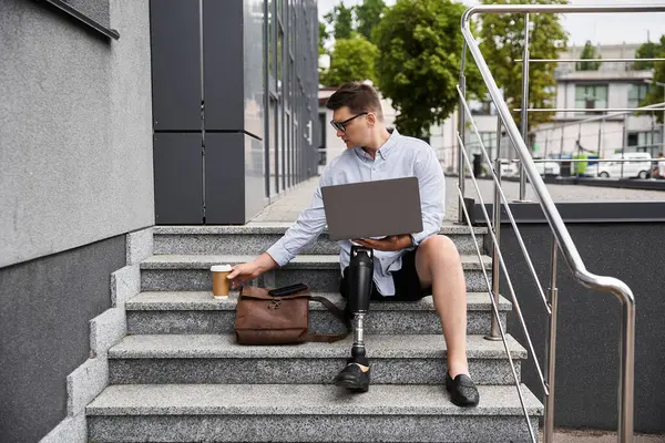 A handsome young man with a prosthetic leg is working on his laptop on outdoor steps. — Stock Photo