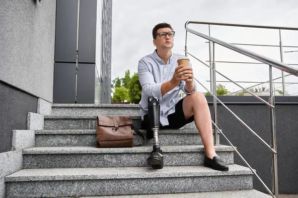 Handsome young man sits on the stairs with coffee, showing his prosthetic leg and relaxed style. — Stock Photo