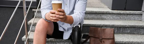 Handsome young man sits on steps, holding coffee cup and showing off prosthetic leg with confidence. — Stock Photo