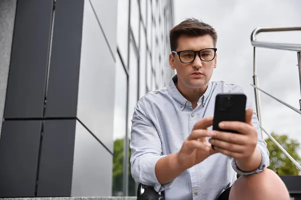 Handsome young man with prosthetic leg looks down at his smartphone while seated outdoors. — Stock Photo