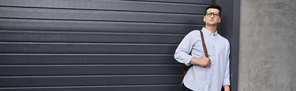 Handsome young man with glasses poses by a sleek garage door in city environment. — Stock Photo