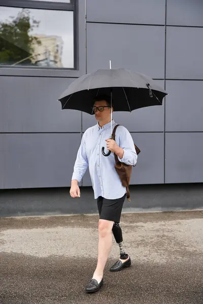 A young handsome man confidently walks with an umbrella while wearing shorts. — Stock Photo
